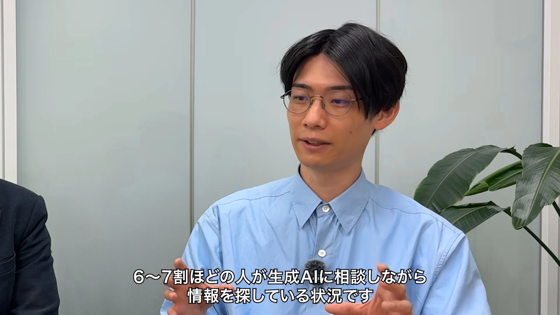 対談動画の場面。青いシャツの人が画面の中央で手を動かして話している。左端にスーツの人の肩が少し見える