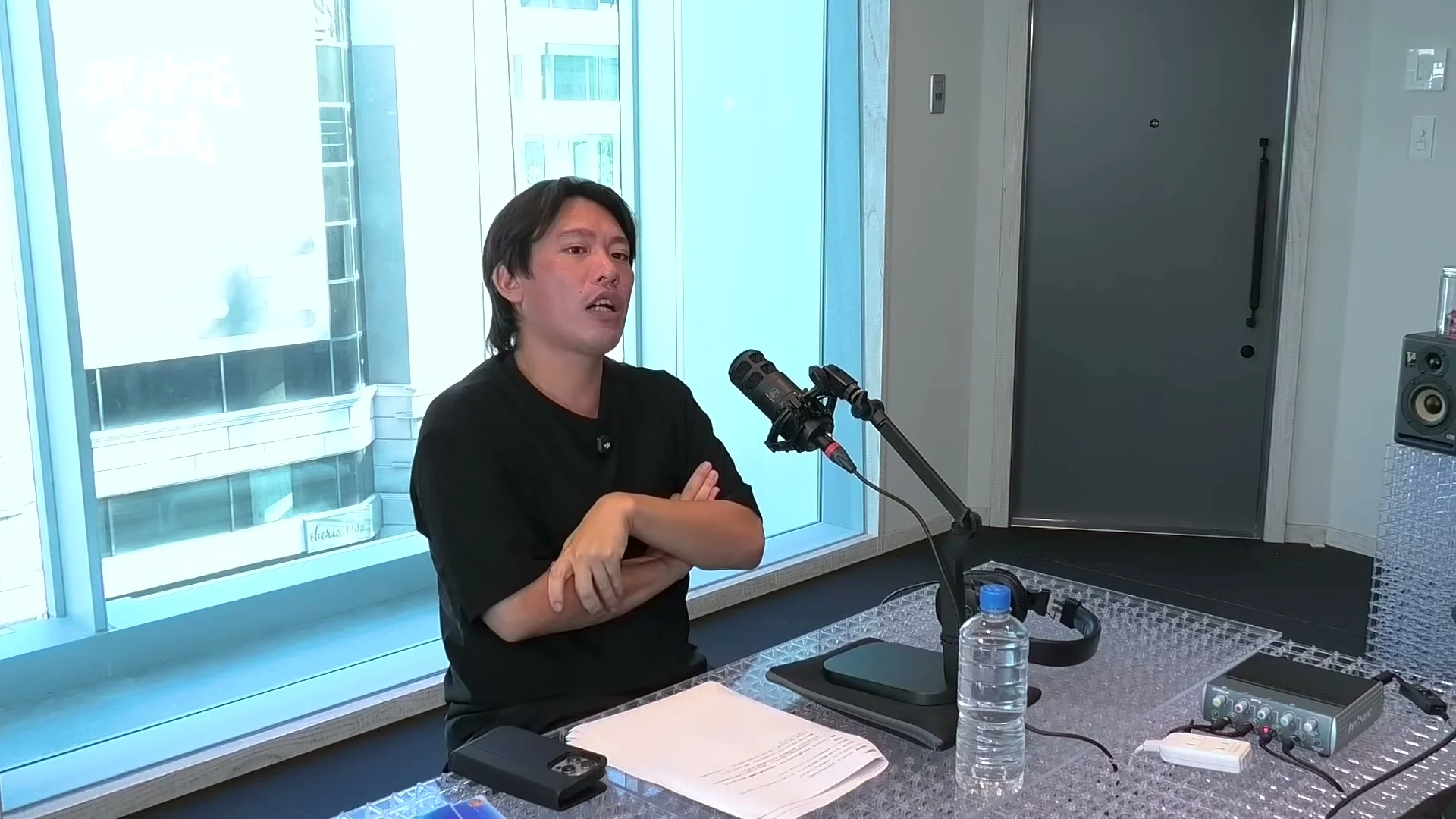 動画キャプチャ: 腕を組んだ出演者が、窓を背に話すアップの場面（16:50頃）