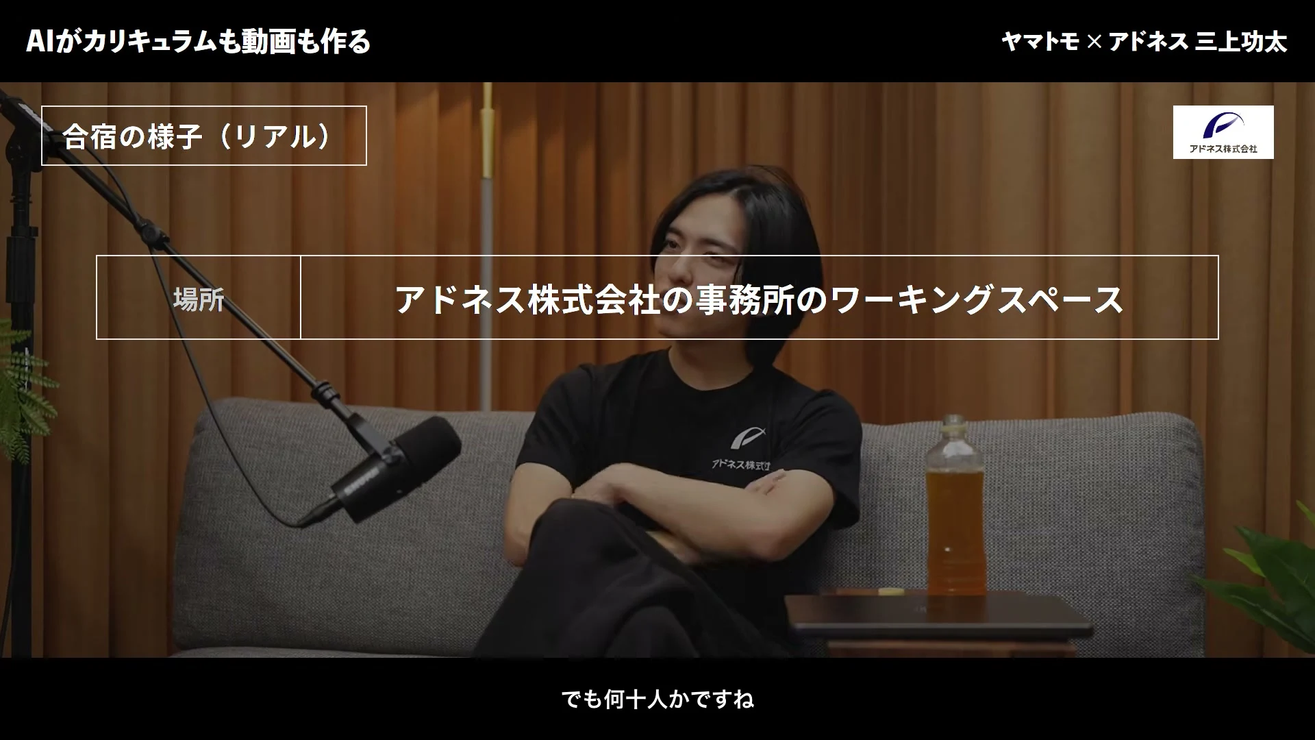 動画キャプチャ: AIがカリキュラムも動画も作る、という画面。合宿の様子として、場所はアドネス株式会社の事務所のワーキングスペース、と出る場面（20:45頃）