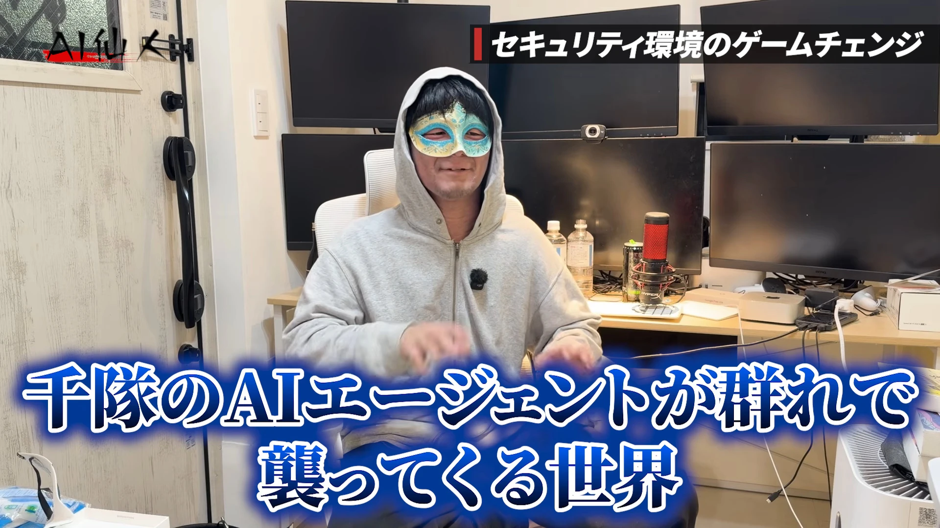 動画キャプチャ。右上にセキュリティ環境のゲームチェンジの帯、下に大きく千隊のAIエージェントが群れで襲ってくる世界の字幕が出て、仙人さんが両手を動かして話す動画の場面
