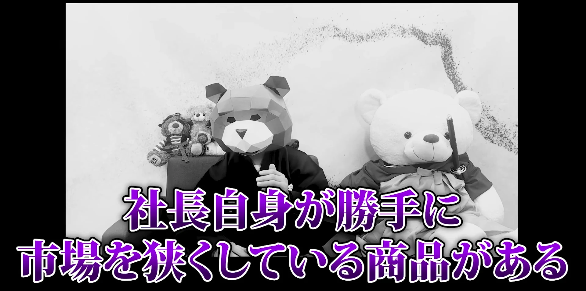 動画の画面。白黒の映像で、熊の被り物をした話し手と白い大きなくまのぬいぐるみが並び、左右に黒い枠。画面下に紫の大きな字で、社長自身が勝手に市場を狭くしている商品がある、と出ている。
