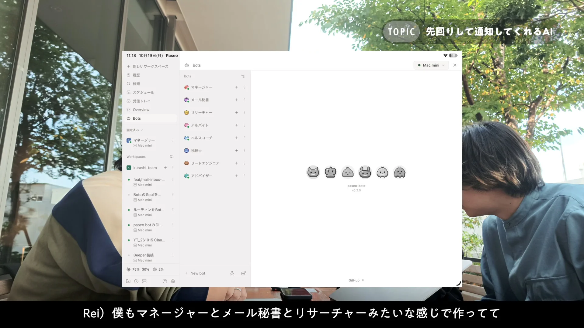 動画の画面。屋外のカフェで話す2人の前に、左にBotsの一覧、中央に6体のドット絵のBotが並ぶ Paseo の画面が重なって映っている場面。一覧にはマネージャー、メール秘書、リサーチャーなどの名前が見える