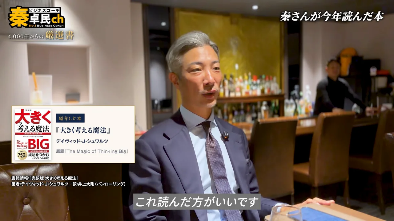 動画の画面。店内で秦卓民さんが話し、左下に『大きく考える魔法』の書影パネルが出ている。右上に、秦さんが今年読んだ本、下のテロップに、これ読んだ方がいいです、と出ている。