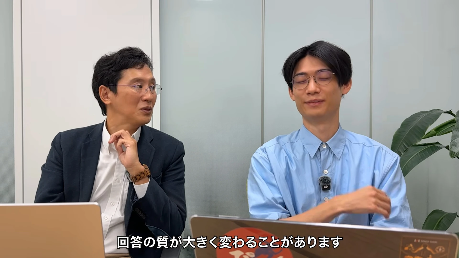 対談動画の場面。左のスーツの人が手を動かして話し、右の青いシャツの人が聞いている