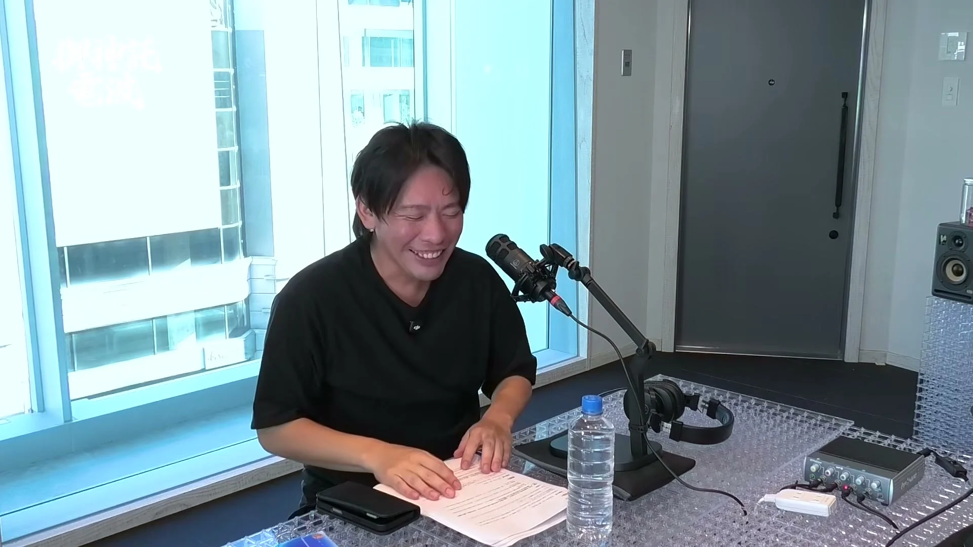 動画キャプチャ: 机をはさんで2人が向き合い、腕を組んだ出演者が話す広角の場面（4:10頃）