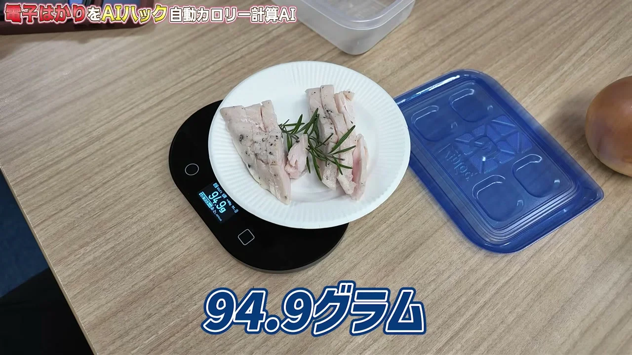 動画キャプチャ: 電子はかりに鶏むね肉の皿を置き、はかりの小さな画面と画面下のテロップに94.9グラムと出る(4:18頃)