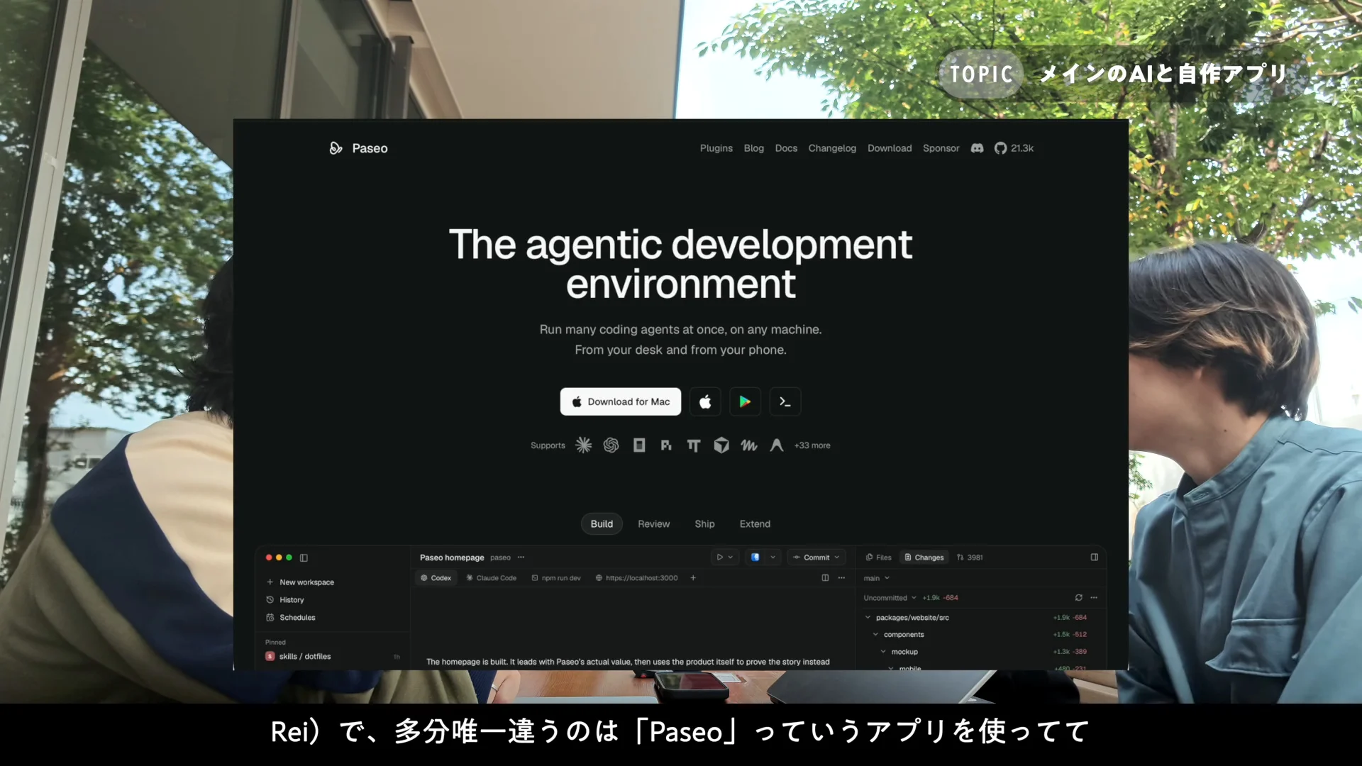 動画の画面。屋外のカフェで話す2人の前に、黒い背景の Paseo の公式サイトが重なって映っている場面。「The agentic development environment」の見出しと、Mac版のダウンロードボタンが見える