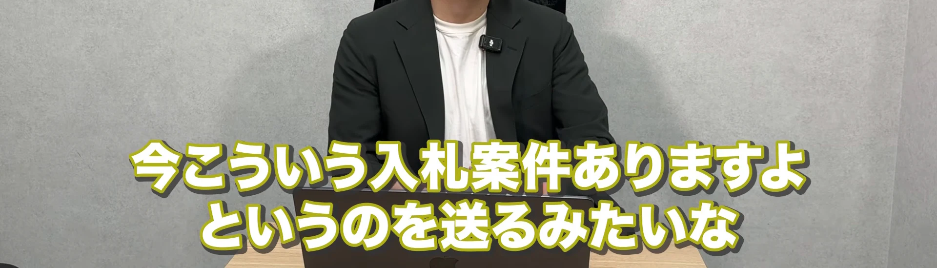 動画の画面。ダークグリーンのジャケットの男性の胸から下と、今こういう入札案件ありますよというのを送るみたいな、と書かれたテロップ。