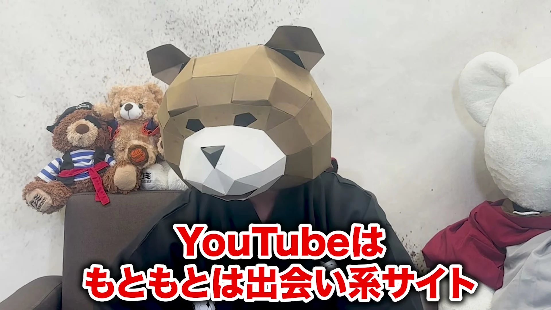 動画の画面。熊の被り物をした話し手が正面を向き、画面下に赤い大きな字で、YouTubeはもともとは出会い系サイト、と出ている。左に熊のぬいぐるみが並ぶ。
