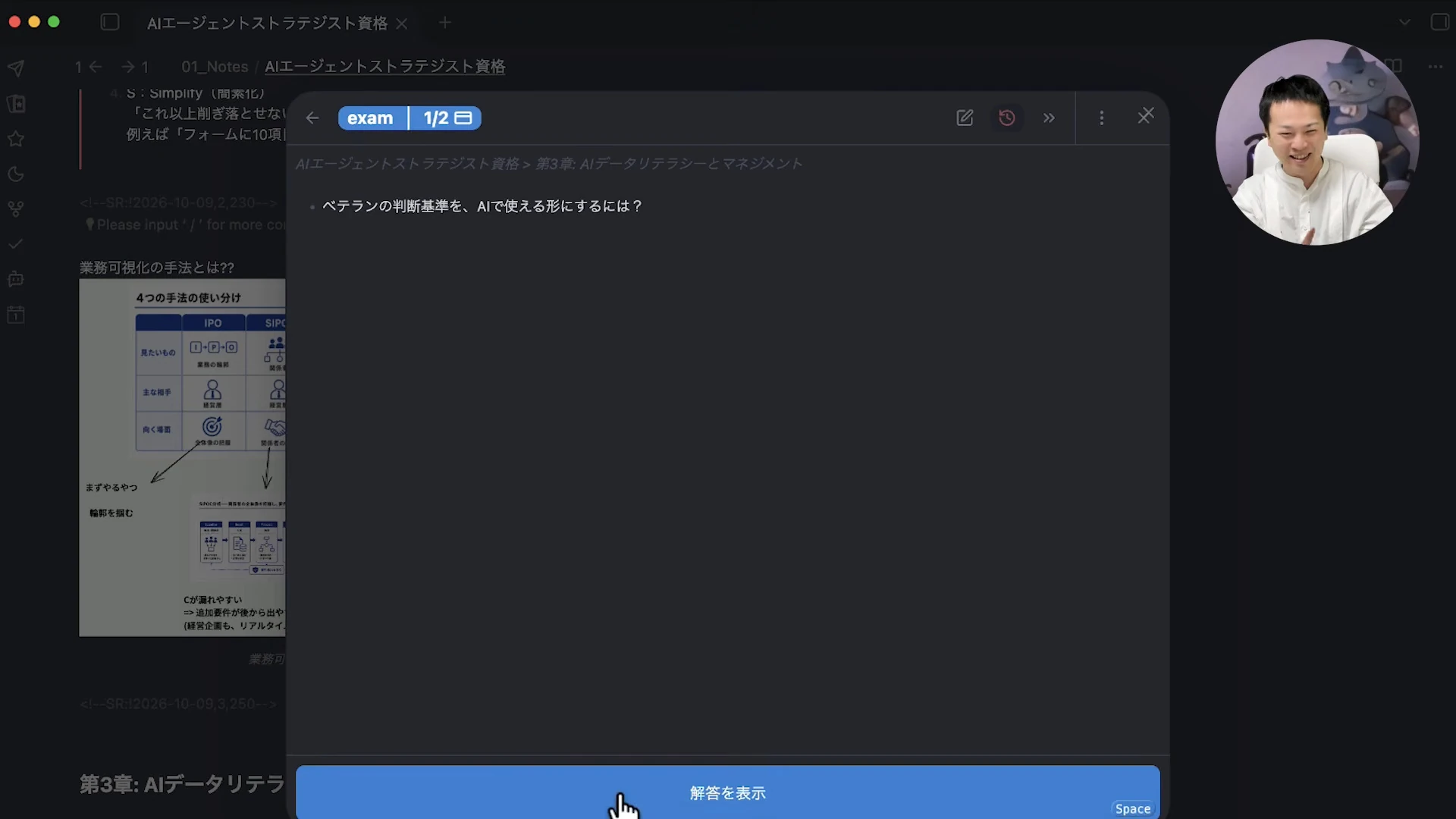 動画の画面。Obsidianのフラッシュカードの復習画面に、「ベテランの判断基準を、AIで使える形にするには?」という問いと、下に「解答を表示」のボタンが映っている場面。背景に業務可視化の図解のノートが薄く見える。右上に笑っている飯塚さんの丸い小窓