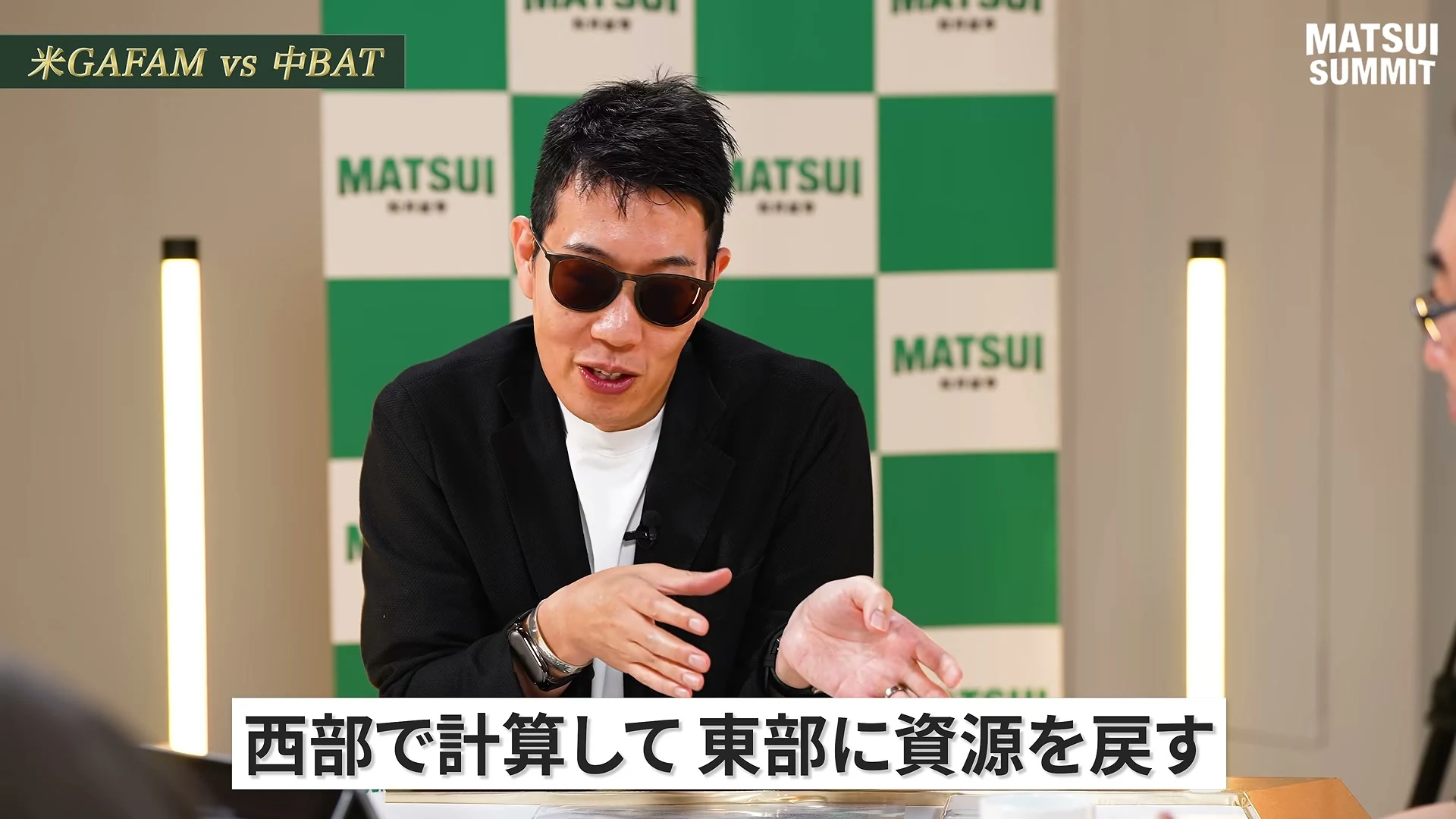 動画の画面。左上に、米GAFAM vs 中BAT、の題。サングラスのものづくり太郎さんが両手を広げて話し、画面下の字幕に、西部で計算して東部に資源を戻す、と出ている。