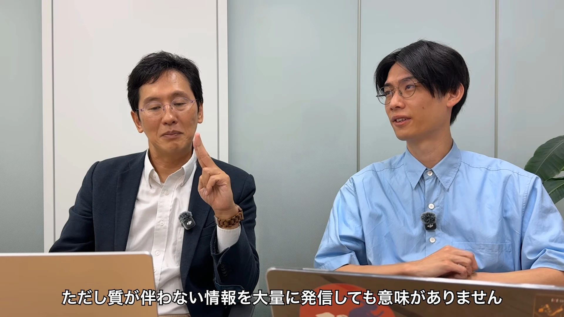 対談動画の場面。左のスーツの人が指を立てて話し、右の青いシャツの人が聞いている