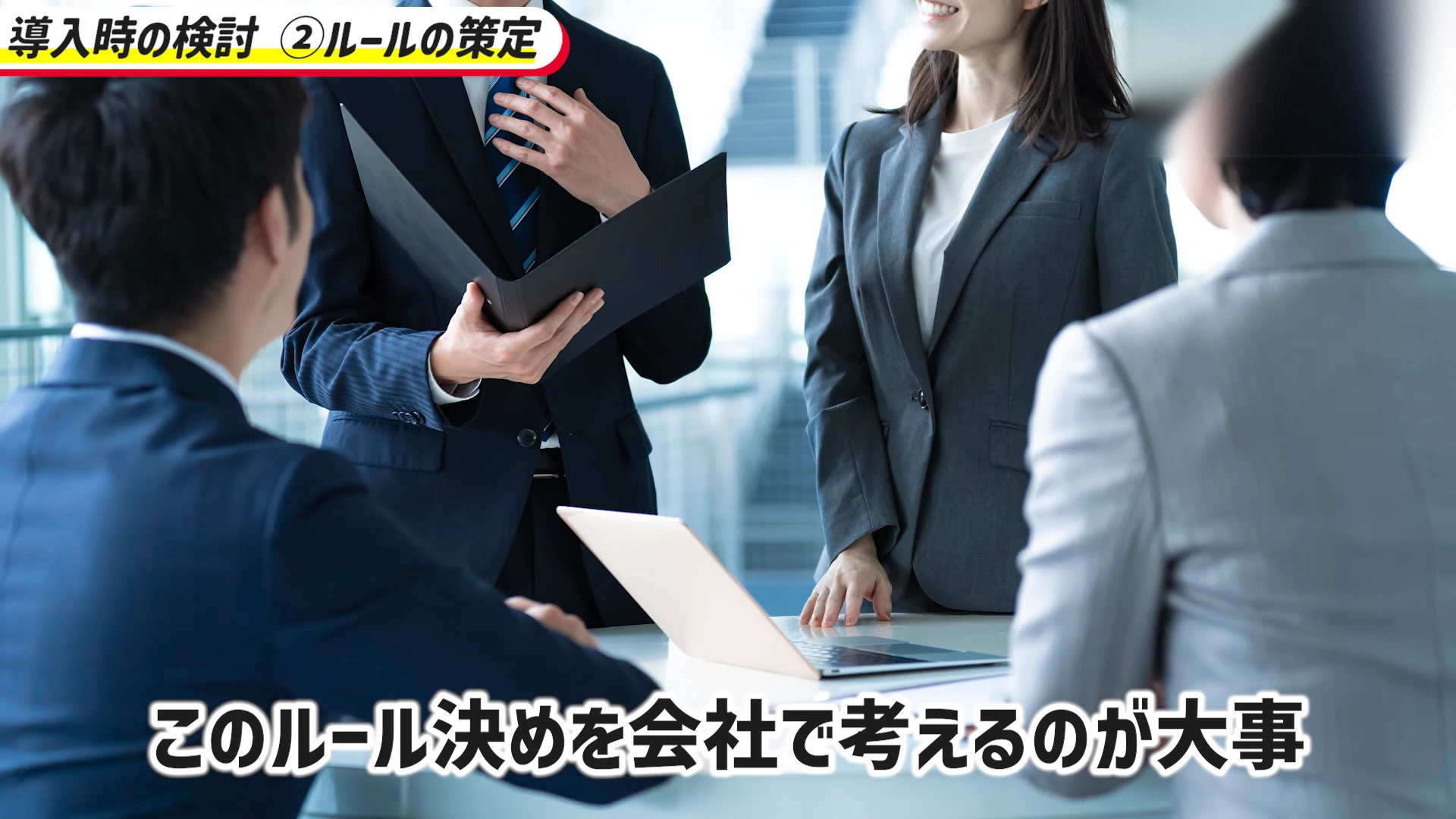 動画の場面。スーツの人たちが書類とノートパソコンを囲んで話し合う写真。字幕は「このルール決めを会社で考えるのが大事」