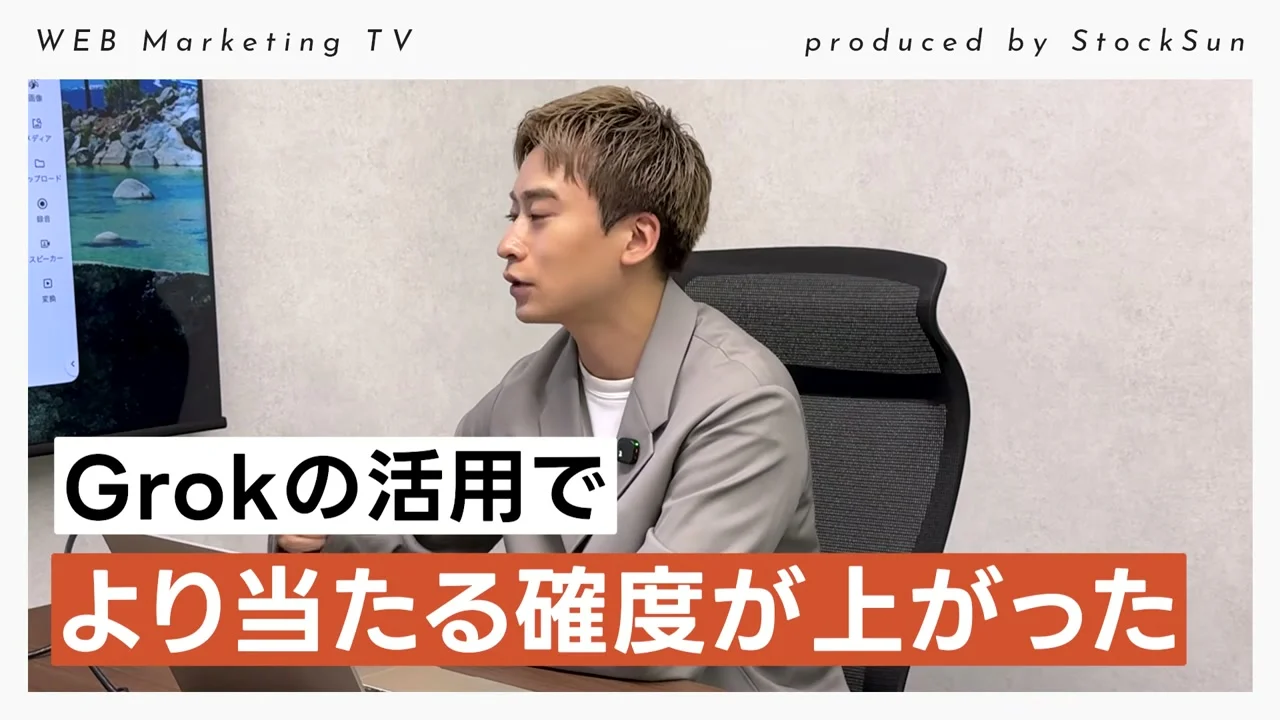 動画キャプチャ: 冒頭の場面。話し手が机に向かって話し、テロップでGrokの活用でより当たる確度が上がった、と出ている（0:10頃）