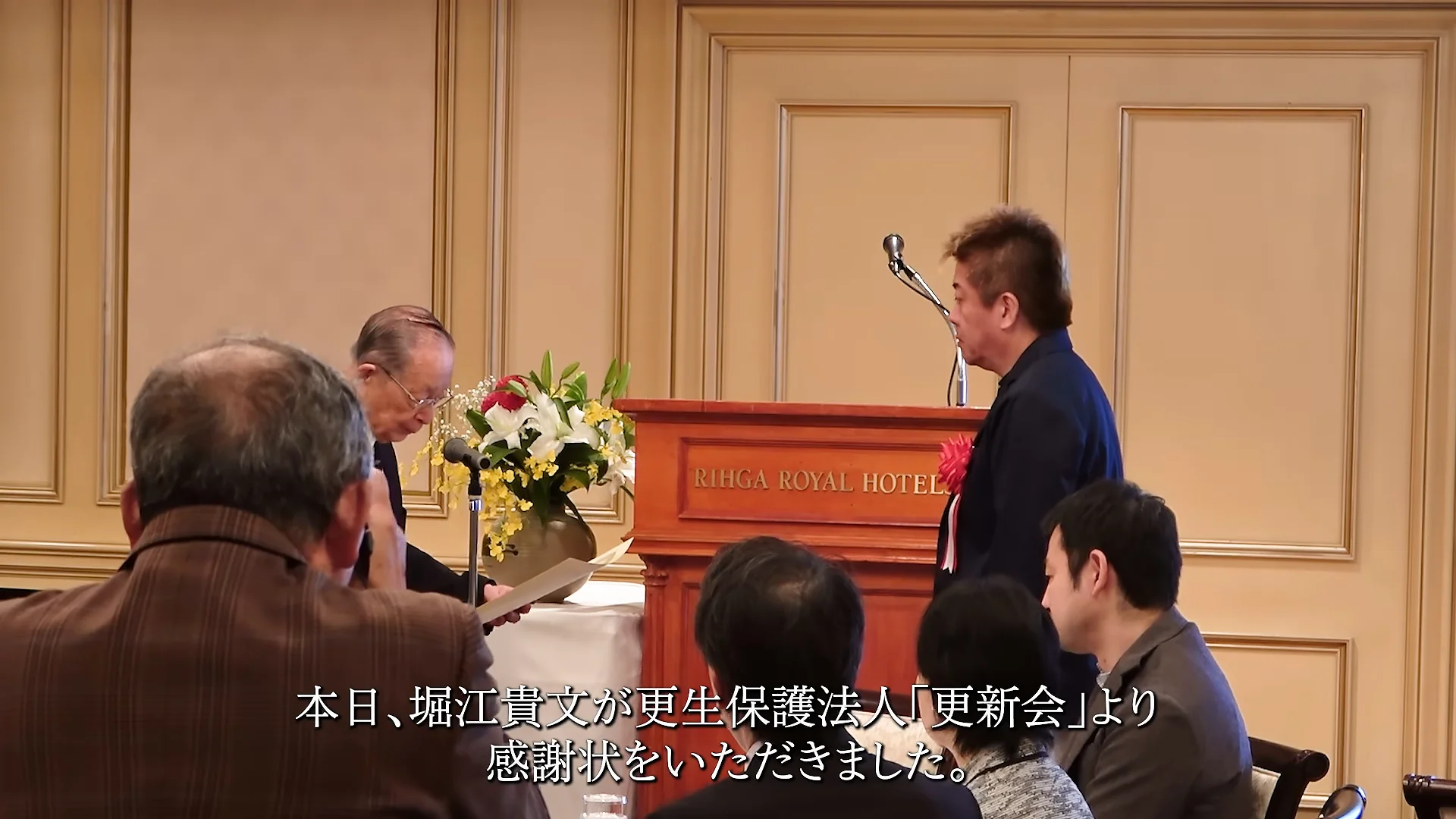 動画の場面: 更生保護法人の更新会で、感謝状を受ける堀江貴文さん(3秒ごろ)