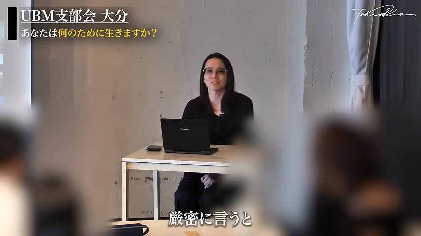 動画キャプチャ: 「厳密に言うと」のテロップが出て、机の前で話し始める場面(7:36頃)