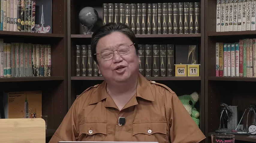 動画キャプチャ: 本棚の前で、岡田さんが笑顔で話している場面（29:10頃）
