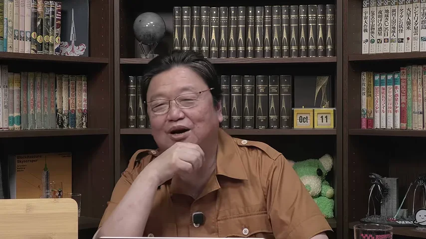 動画キャプチャ: 本棚の前で、岡田さんが手をあごに当てて話している場面（30:16頃）