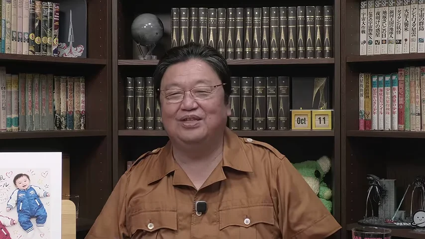 動画キャプチャ: 本棚の前で、岡田さんが笑顔で話している場面。左下にベビー服の広告が見える（35:54頃）